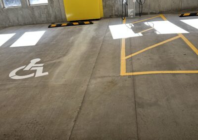 A parking garage with a marked accessible parking space next to an electric vehicle charging station and yellow painted barriers.
