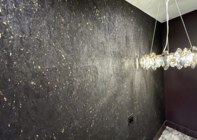 Textured dark wall with subtle gold flecks; a modern chandelier with glass elements hangs from the ceiling on the right side.